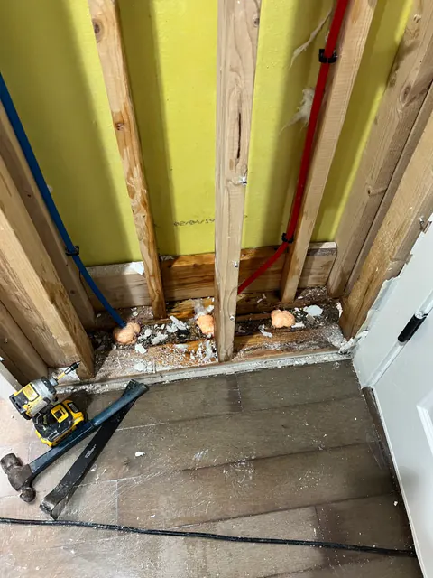 Bathroom wall opened to the studs with red and blue supply lines capped for testing