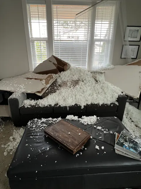 Fallen ceiling drywall and wet insulation covering a sofa and leather ottoman