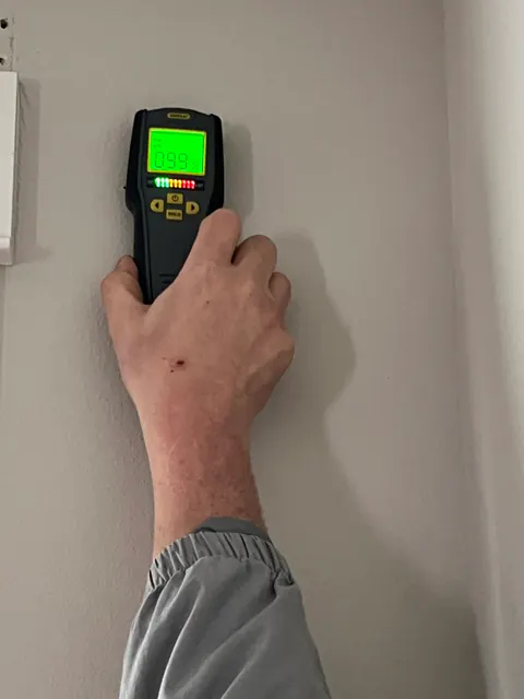 Pinless moisture meter reading 99 percent on a painted wall