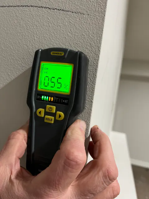Moisture meter reading 55 percent on drywall next to a corner
